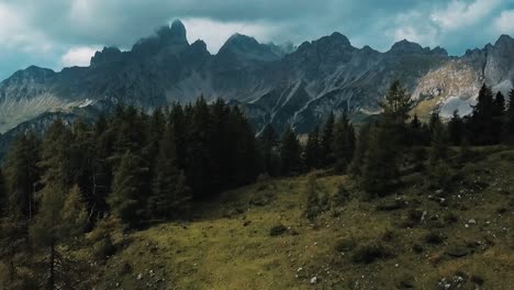 A-drone-shot-crests-a-wooded-hill-to-reveal-the-majestic-Alps-mountain-range-in-Austria