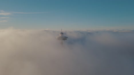 Elevator-descends-tall-iconic-structure-shrouded-in-misty-fog,-aerial-dolly