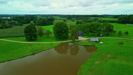 Green-fields-and-dirty-water-pond-in-countryside-landscape,-aerial-view