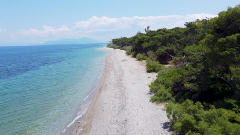 A-drone-flies-parallel-to-an-empty,-pristine-beach-along-the-Greek-coastline