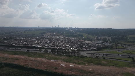 In-this-4K-aerial-footage,-a-push-in-shot-approaches-the-bustling-city-of-Johannesburg,-framing-a-busy-highway-and-township,-providing-a-dynamic-glimpse-into-urban-energy-and-daily-life