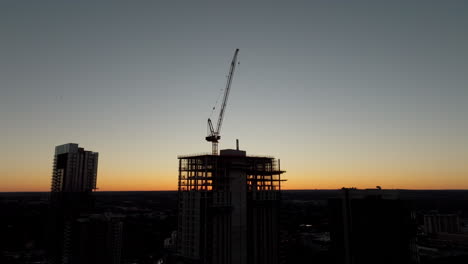 Crane-silhouetted-on-top-of-skyscraper-construction-at-sunset