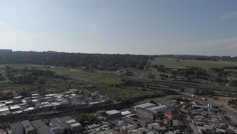 Push-in-drone-shot-glides-over-the-township-of-Alexandra-in-Johannesburg-as-a-high-speed-train-swiftly-passes-by,-offering-a-glimpse-of-the-energetic-cityscape-and-rapid-transportation-in-motion