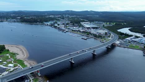 Drone-aerial-shot-over-Batemans-Bay-bridge-cars-highway-with-rural-town-shops-commercial-infrastructure-Clyde-river-South-Coast-Australia