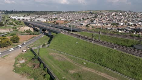In-this-concise-4K-aerial-footage,-a-rising-drone-captures-the-urban-landscape-of-a-township-adjacent-to-the-Gautrain-railways-and-highways-in-Johannesburg,-South-Africa