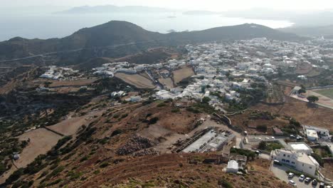 Drone-view-in-Greece-flying-over-a-white-church-on-a-hill-with-a-greek-white-house-town-facing-blue-sea-on-a-mountain