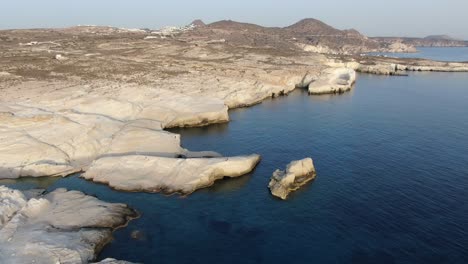 Drone-view-in-Greece-flying-over-a-moon-shaped-white-rock-area-in-Milos-island-at-sunrise-next-to-the-dark-blue-sea