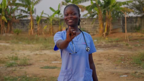 Black-African-female-doctor-nurse-in-blue-lab-cost-with-stethoscope-saying-ove-with-hand-gesture-language-smiling-in-front-of-camera