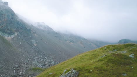 Toma-Aérea-Adelantando-Una-Colina-Verde-Para-Descubrir-El-Valle-De-Montaña-Con-Niebla-En-Los-Alpes