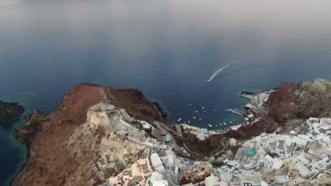 Vista-De-Drones-En-Grecia-Volando-Sobre-Santorini-Con-Casas-Blancas-De-La-Ciudad-De-Oia-Y-Techos-Azules-En-Un-Acantilado-Junto-Al-Mar-Mediterráneo-Al-Amanecer