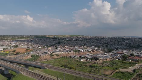 Drone-footage,-a-climbing-shot-captures-the-cityscape-of-Johannesburg,-ascending-over-a-township-and-railway,-offering-a-compelling-view-of-the-urban-landscape-and-transportation-infrastructure