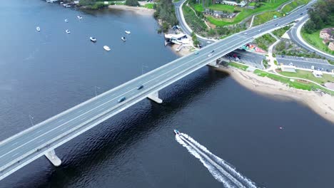 Drone-aerial-cars-traffic-passing-over-highway-with-boat-on-river-transport-infrastructure-Clyde-River-Batemans-Bay-South-Coast-Australia