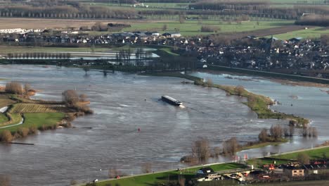 Aerial-panning-shot-of-the-Lek-River-overrunning-its-banks-with-the-town-of-Nieuwegein-in-the-background-and-a-freighter-trying-to-make-its-way-along-the-river