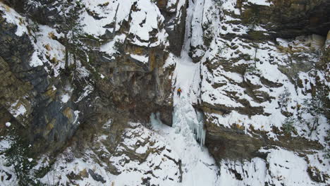 Drone-shot-reveals-landscape-of-Annapurna-circuit-Nepal,-Trekker-climbs-frozen-Waterfall-at-snowy-weather-Manang,-adventurous-tourism-experience-4K