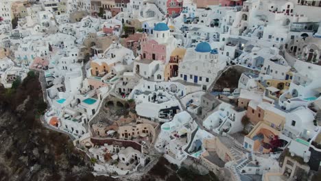 Vista-De-Drones-En-Grecia-Volando-Sobre-Santorini-Con-Casas-Blancas-De-La-Ciudad-De-Oia-Y-Techos-Azules-En-Un-Acantilado-Junto-Al-Mar-Mediterráneo-Al-Amanecer