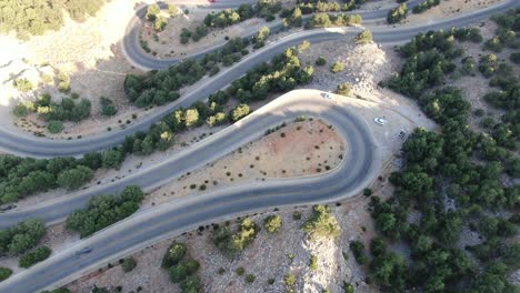 Drone-view-in-Greece-flying-over-a-brown-and-green-mountain-with-serpent-road-and-sea-on-the-horizon-on-a-sunny-day-top-view