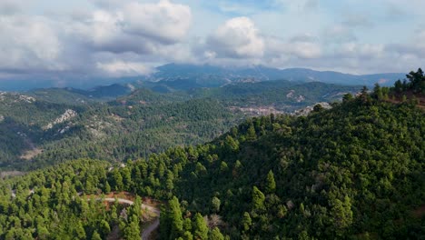 Drone-View-Over-a-Green,-Lush-Forest-With-Tall-Mountain-Peaks-and-a-Clear-Blue-Sky-With-Thick-White-Clouds,-Evia-Island,-Greece