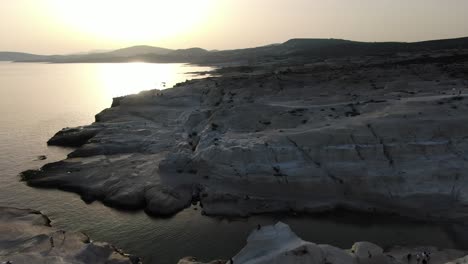 Drohnenansicht-In-Griechenland,-Die-Bei-Sonnenaufgang-über-Einem-Mondförmigen-Weißen-Felsengebiet-Auf-Der-Insel-Milos-Neben-Dem-Dunkelblauen-Meer-Fliegt