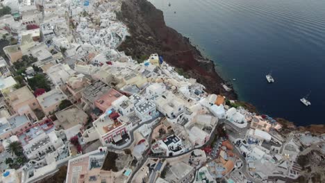 Drone-view-in-Greece-flying-over-Santorini-with-Oia-town-top-view-white-houses-and-blue-roofs-on-a-cliff-next-to-the-mediterranean-sea-at-sunrise