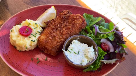 Delicious-deep-fried-fish-with-mashed-potatoes-and-salad-on-a-red-plate,-seafood,-4K-shot