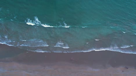 Aerial-view-of-gentle-waves-hitting-a-sandy-beach-from-the-top-view