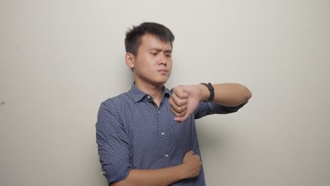 Studio-shot-of-young-asian-man-waiting-impatiently-watching-clock-in-Blue-shirt