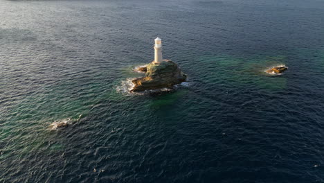Aerial-view-video-of-iconic-lighthouse-in-Andros-island-chora,-Cyclades,-Greece-at-dusk