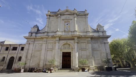 Large-house-front-of-a-church-with-stone-columns-and-a-large-clock-in-strong-sunshine-in-a-historical-place