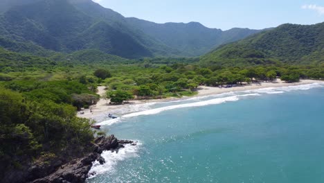 Serene-beach-with-anchored-boats-at-Tayrona-National-Park,-surrounded-by-lush-mountains