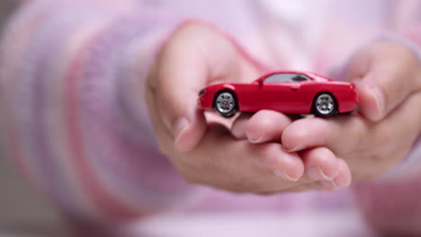 Eine-Frau-In-Der-Hand,-Die-Ein-Rotes-Spielzeugauto-Hält,-Steht-Für-Sicherheit-Bei-Automobilinvestitionen
