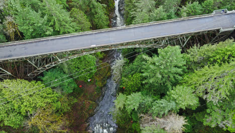 4K-drone-footage-flying-down-to-river-in-evergreen-forest-overlooking-bridge