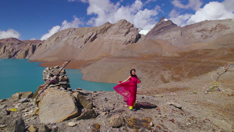 Nepali-female-actress-feels-air-at-World's-highest-altitude-Lake-Nepal-Tilicho,-Drone-shot-reveals-landscape-of-Annapurna-region,-pink-dress-flaunting-in-Mountain-4K