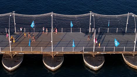 Tourists-walk-across-Queen-Emma-pontoon-bridge-with-festive-flags-and-railing
