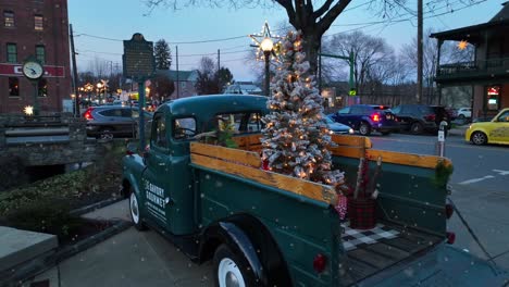 Vintage-truck-with-a-Christmas-tree-in-the-bed,-adorned-with-lights,-in-the-quaint,-festive-evening-setting-of-Lititz,-Pennsylvania