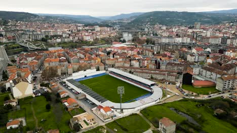 Un-Dron-Asciende-Para-Revelar-Un-Estadio-De-Fútbol-Cerca-De-Los-Puentes-Y-El-Río-De-Ourense-Al-Mediodía