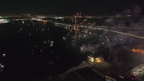 Aerial-view-showing-spectacular-firework-at-night-with-river-and-bridge-in-background---Fort-Myers,-Florida,-USA
