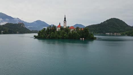 Crane-down-drone-shot-of-Lake-Bled,-Slovenia-in-the-morning-during-summer-time