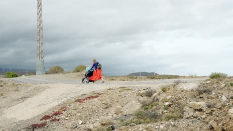 Young-adventurous-mother-struggling-with-stroller-on-harsh-Tenerife-landscape