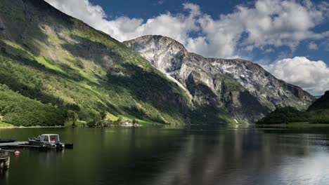 Heavy-clouds-move-fast-above-the-calm-Norwegian-Naeroy-fjord-and-forest-covered-mountains,-casting-dark-shadows