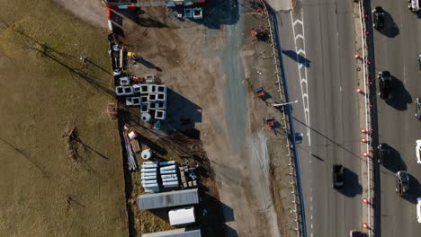 A-top-down-view-of-a-construction-site-with-equipment-and-vehicles-parked-by-the-Belt-Parkway-and-a-park-in-Brooklyn,-NY-on-a-sunny-day