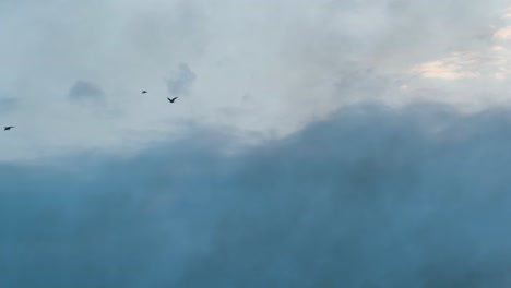 Pequeña-Bandada-De-Cuervos-Siluetas-Volando-A-Través-Del-Cielo-Azul-Nublado