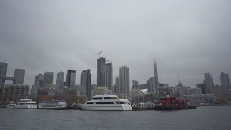 Shot-of-a-cruise-ship-parked-at-a-harbor-with-beautiful-skyline-of-Downtown,-Toronto-at-foggy-evening-in-Canada