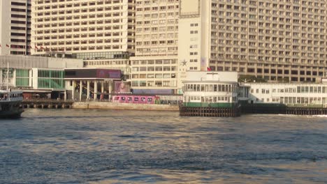 Toma-De-Un-Ferry-Estrella-Saliendo-Del-Puerto-Durante-La-Tarde-Con-Edificios-Al-Fondo-En-Tsim-Sha-Tsui,-Hong-Kong.