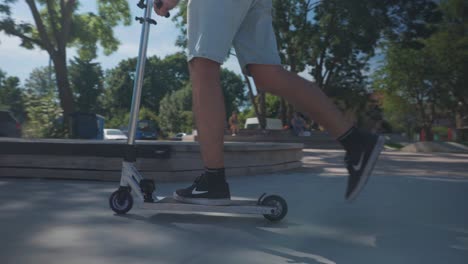 Person-in-shorts-ride-silver-color-stunt-scooter-at-local-public-skatepark