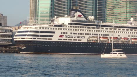 Foto-De-Un-Crucero-Gigante-Estacionado-Junto-A-Un-Puerto-Con-Otros-Barcos-Y-Cruceros-Durante-El-Día-En-Tsim-Sha-Tsui,-Hong-Kong.
