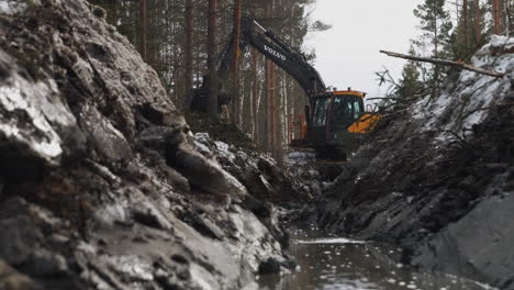 construction-worker-uses-an-excavator-to-move-dirt,-clearing-land,-in-the-forest-near-water