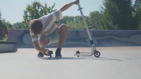 Man-with-stunt-scooter-put-action-camera-on-skatepark-concrete-ground