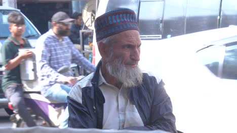 Closeup-slow-motion-shot-of-an-old-man-wearing-jacket-staring-at-something-during-afternoon-at-Saddar-Bazar-Street-of-Karachi,-Pakistan