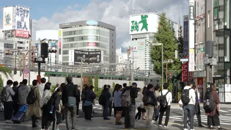 Gente-Esperando-En-El-Cruce-De-Peatones-En-La-Plaza-De-La-Estación-De-Salida-Este-De-Shinjuku-Jr-Con-Paisaje-Urbano-En-Segundo-Plano