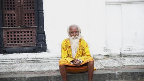 Frontal-view-of-old-hermit-sacred-man-in-yellow-robes-against-white-wall-on-side-of-road